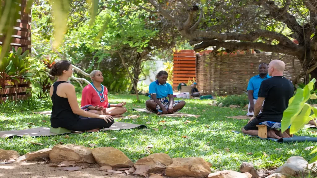 People meditate together with MindWise Retreats in the lush tropical gardens of Bahia Mar Boutique Hotel, surrounded by palm trees, greenery, and a peaceful coastal atmosphere in Vilanculos
