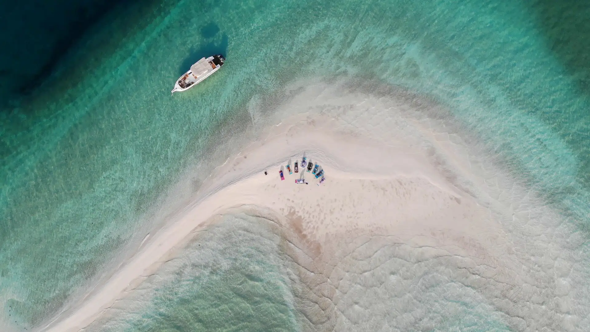 A group of people practicing yoga and meditation on a pristine sandbank surrounded by turquoise waters in the Indian Ocean off the coast of Vilanculos, Mozambique, with clear skies and a tranquil tropical setting