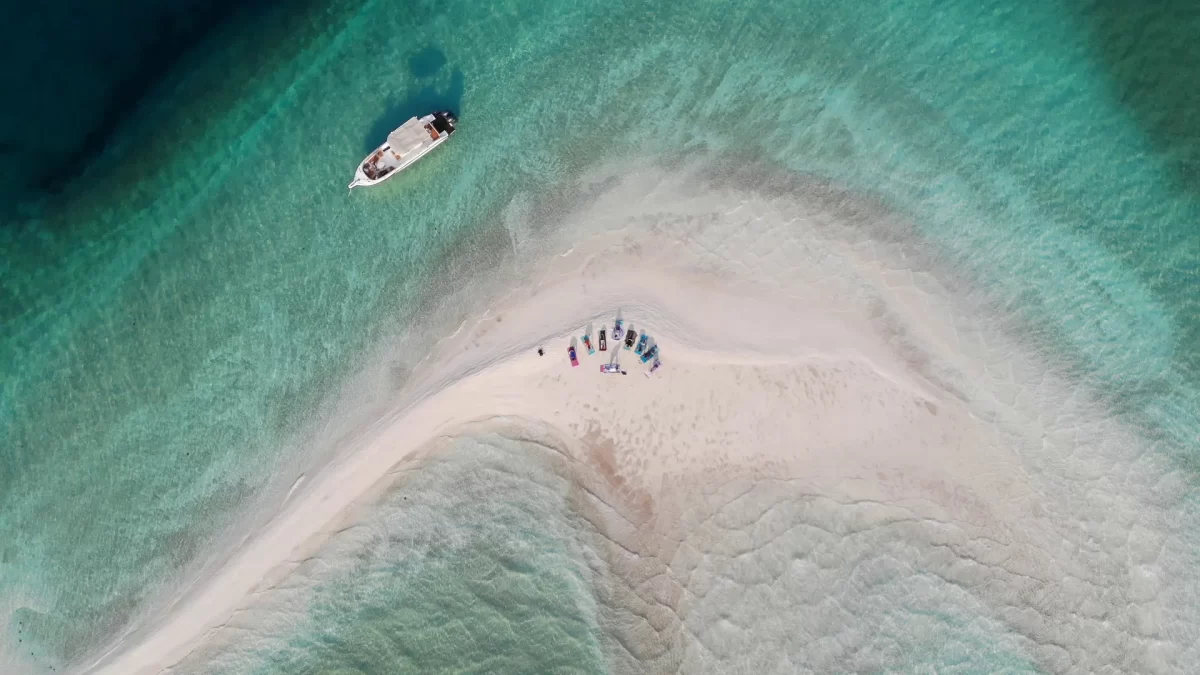 A group of people practicing yoga and meditation on a pristine sandbank surrounded by turquoise waters in the Indian Ocean off the coast of Vilanculos, Mozambique, with clear skies and a tranquil tropical setting